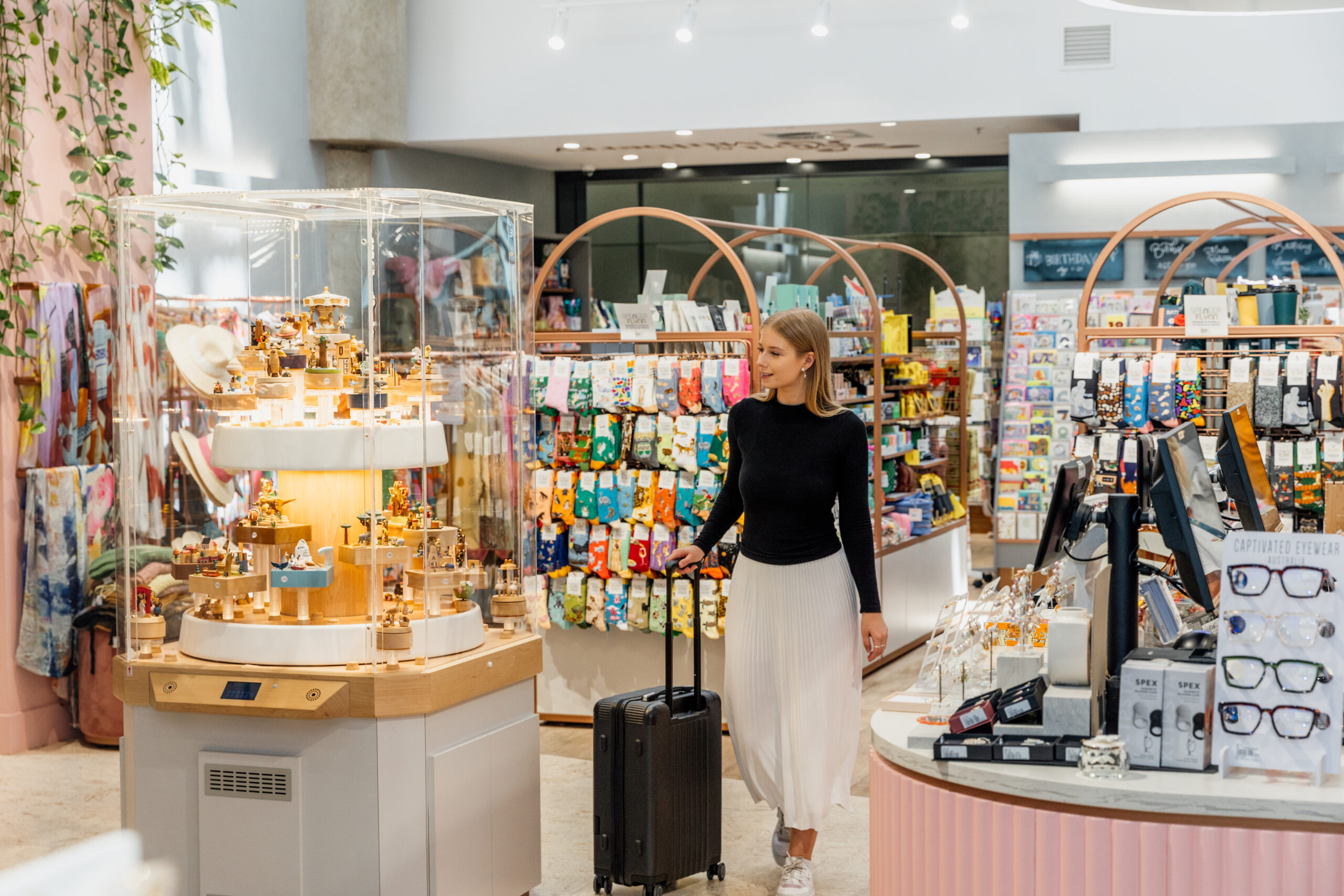 Young woman browsing store in airport while pulling a bag