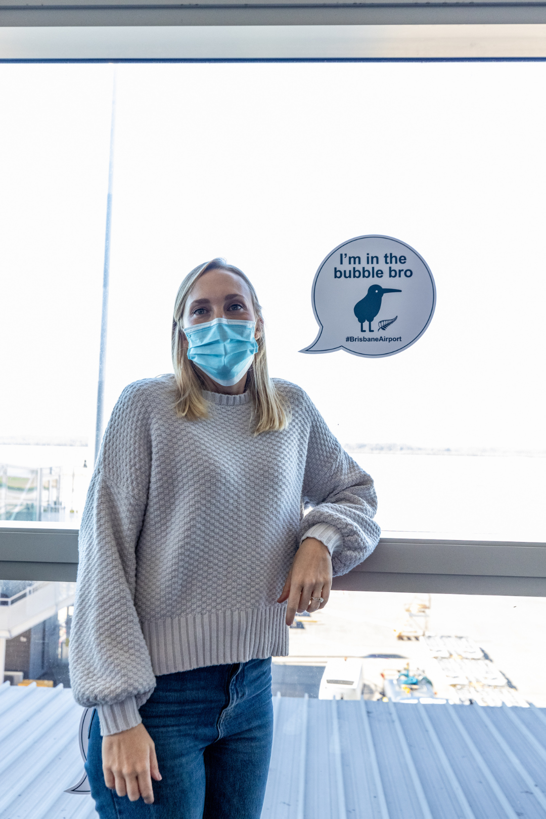 Woman wearing face mask standing next to a sticker on window