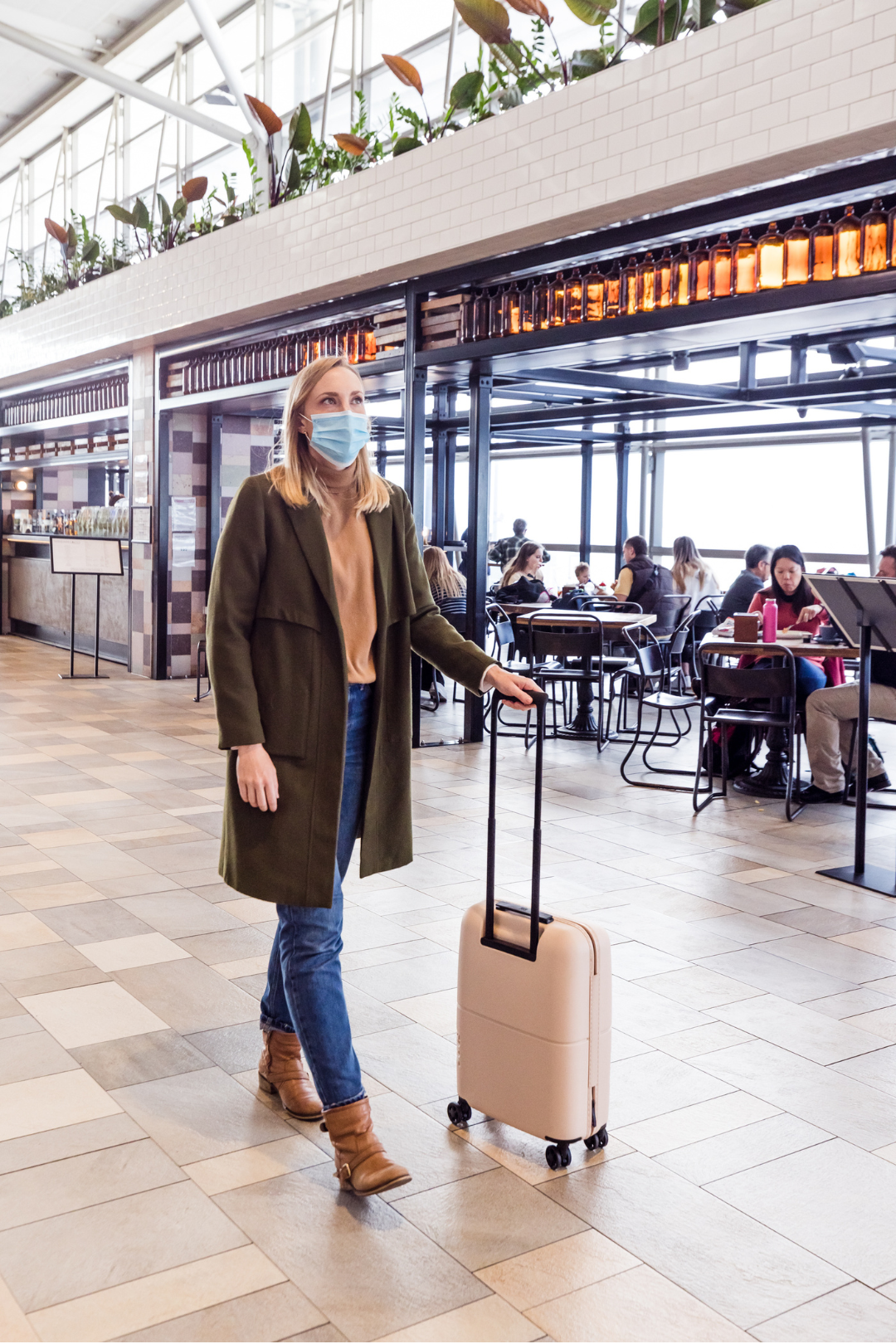 Woman wearing mask walking through airport with suitcase